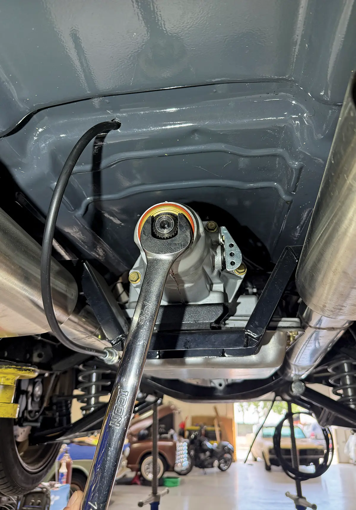 Mechanic tightening a yoke nut on the transmission output shaft using a large chrome wrench, essential for installing a custom driveshaft.