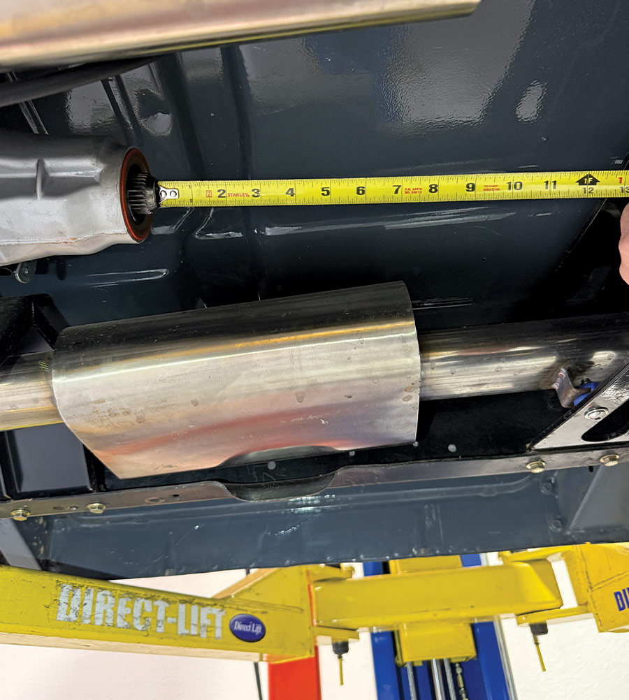 Technician using a tape measure to determine the required driveshaft length, measuring from the transmission output seal to a midpoint on the chassis.