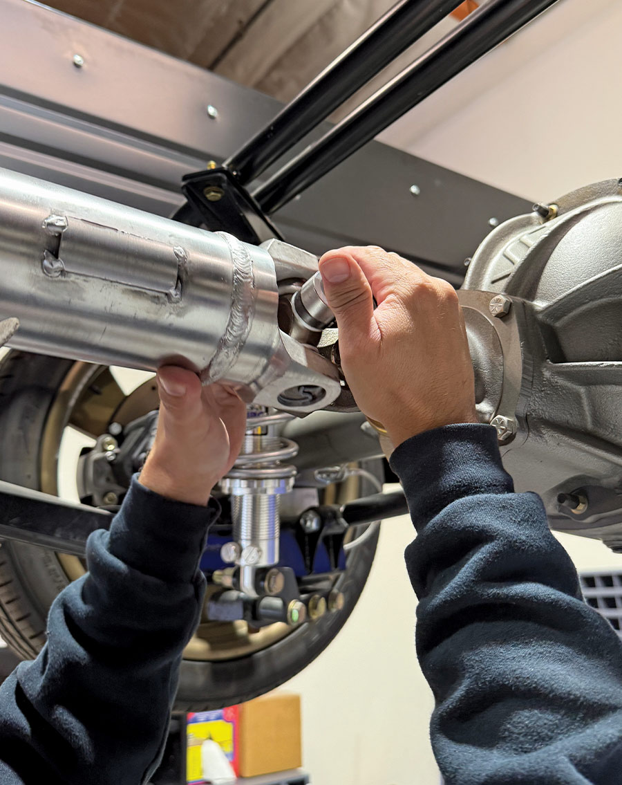 Technician aligning and installing the driveshaft U-joint yoke onto the rear differential flange of a performance truck with coil-over shocks.