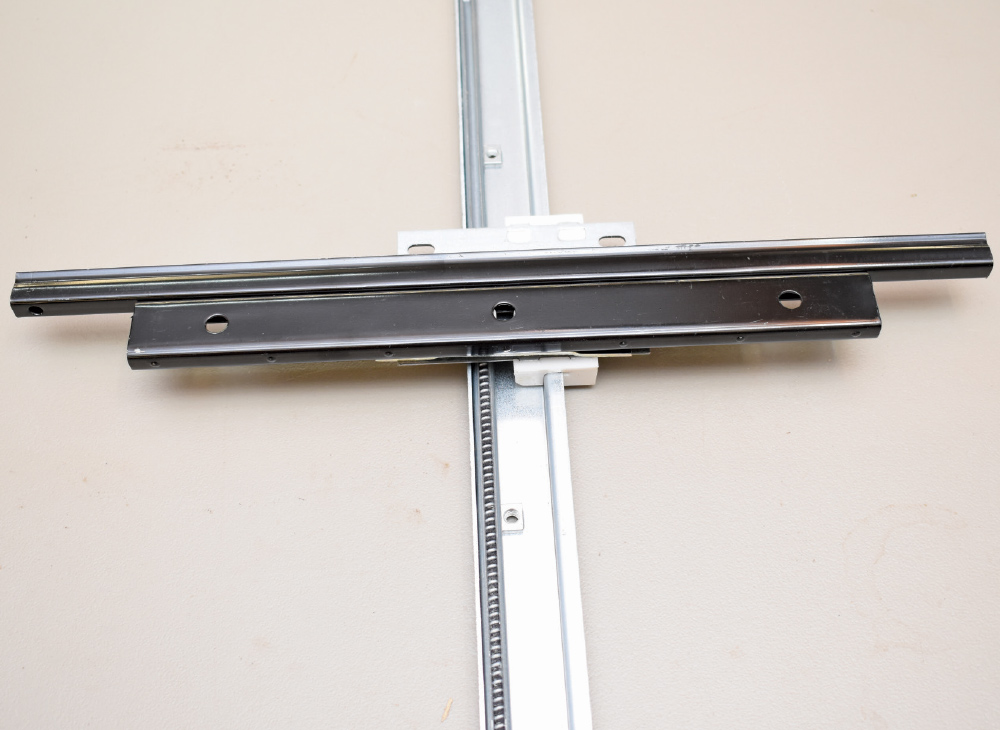 A power window regulator track assembly, featuring two black metal guide rails lying on the silver toothed track.