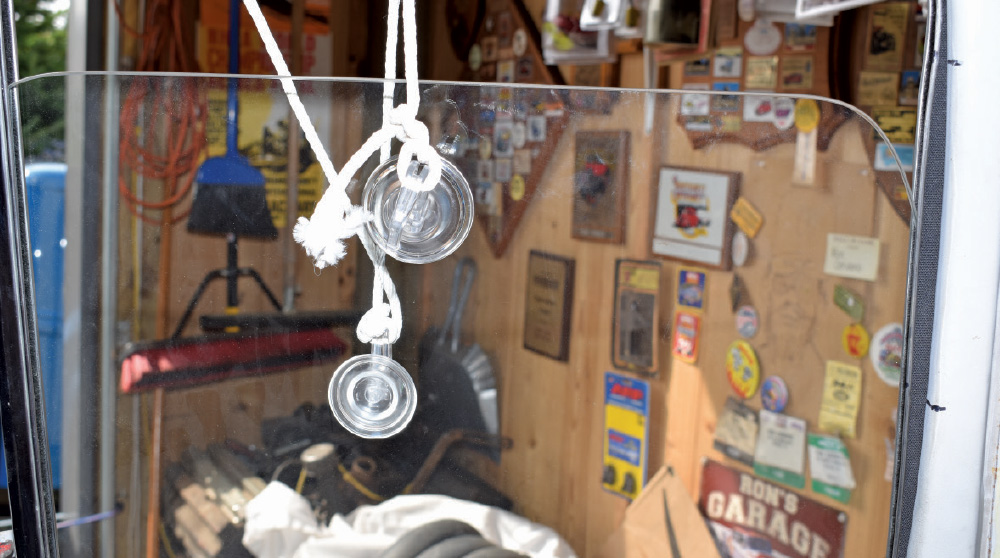Car window glass held by two suction cups and a white rope, positioned in front of a cluttered garage work area.