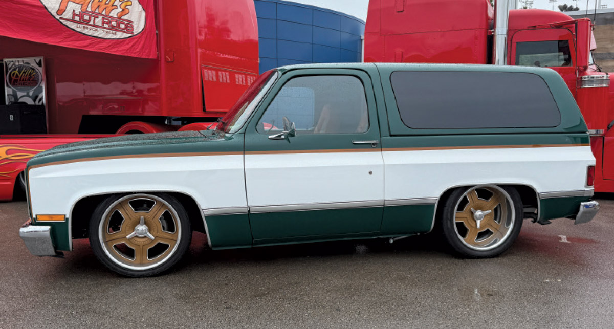  A side view of a green and white lowered K5 Blazer with gold-finished custom wheels, parked at an event.