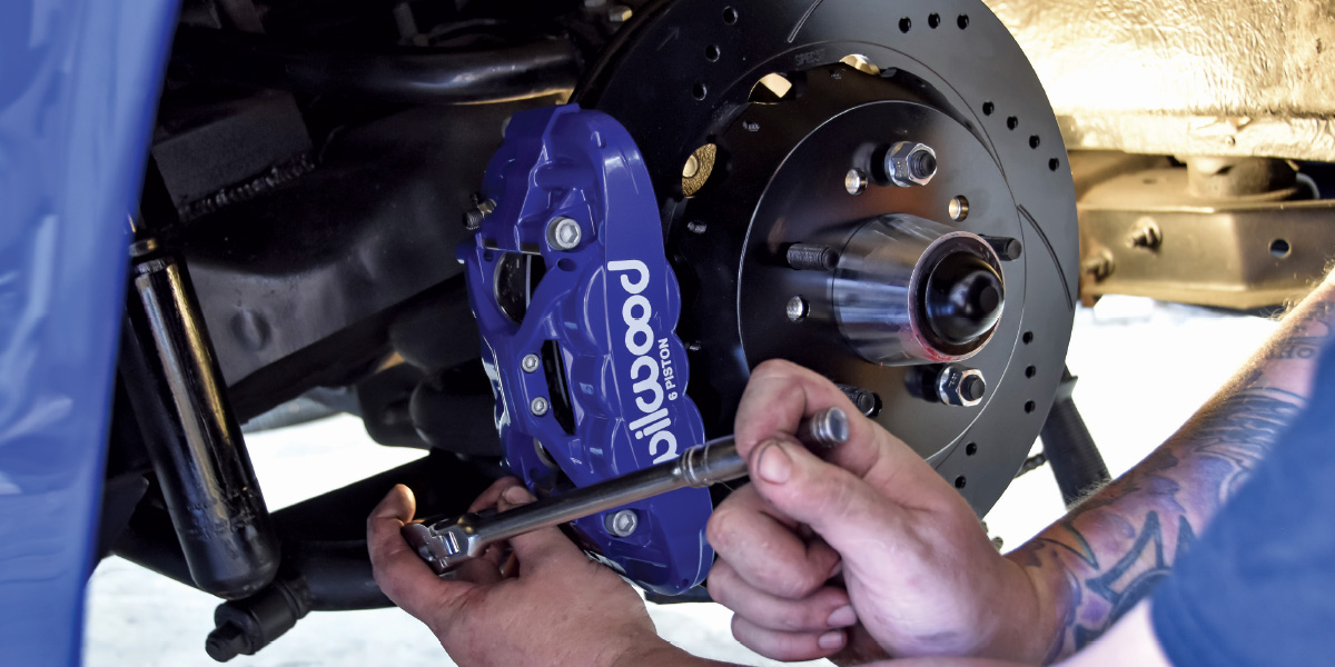 Blue Wilwood caliper mounted to black bracket with drilled performance rotor visible