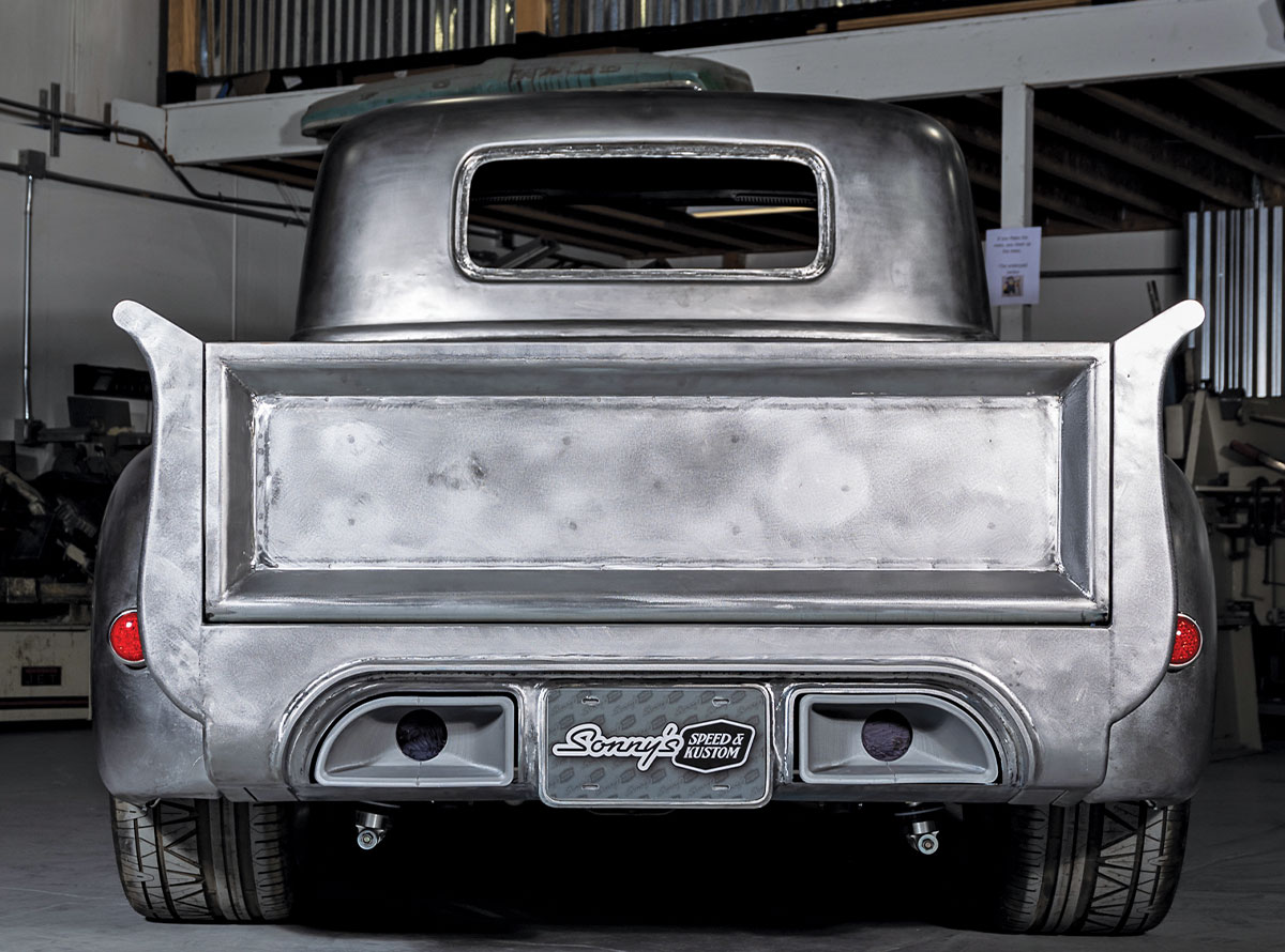 Rear view of a bare-metal Chevrolet 3100 truck featuring a smooth tailgate and flared fenders. The lower rear panel includes integrated dual exhaust ports and a "Sonny’s Speed & Kustom" license plate.