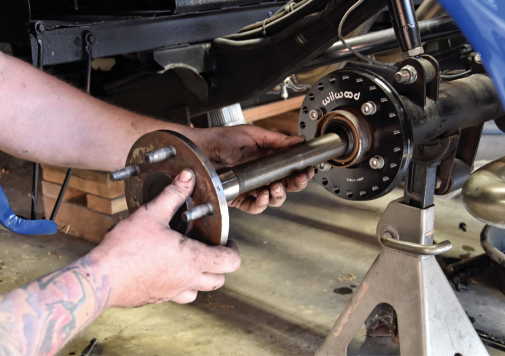 Hands sliding a metal axle shaft into an axle housing fitted with a black Wilwood adapter plate.