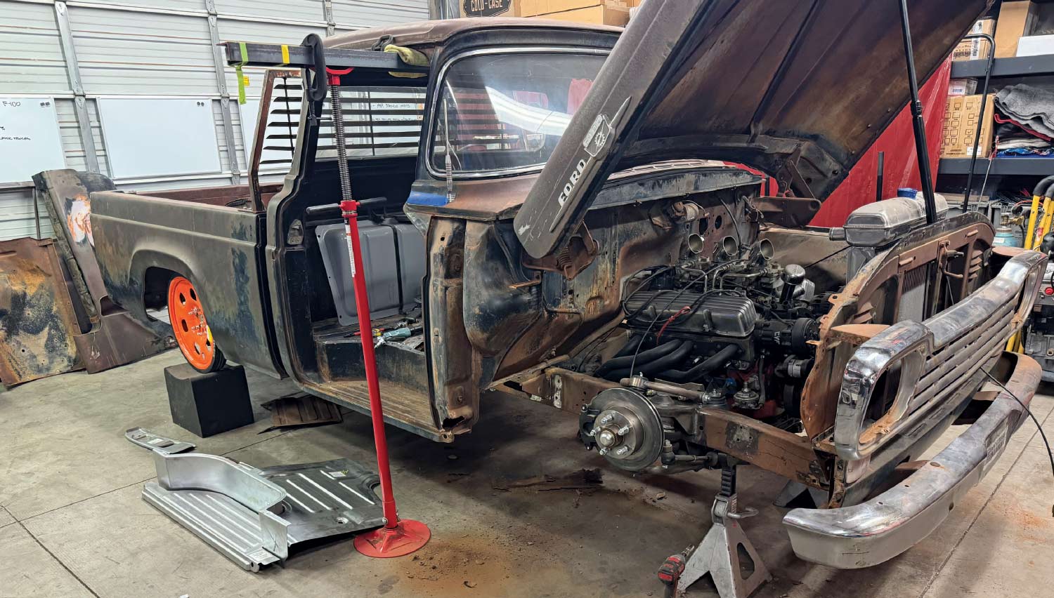 A vintage Ford truck chassis in a workshop undergoing extensive metal restoration with new floor and suspension components visible.
