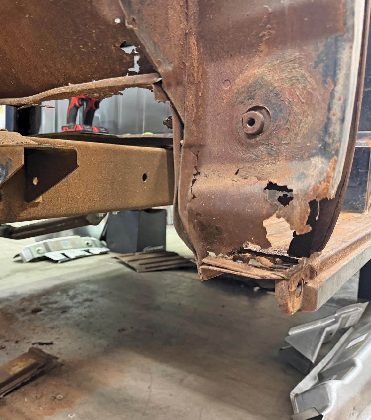A severely rusted lower cab corner and floor support section on a vintage truck before being repaired.