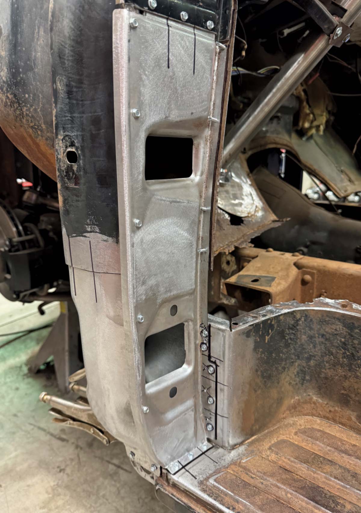 Close-up of a new steel inner door post panel precisely aligned and bolted onto a restored truck pillar, with marker lines for final trimming.