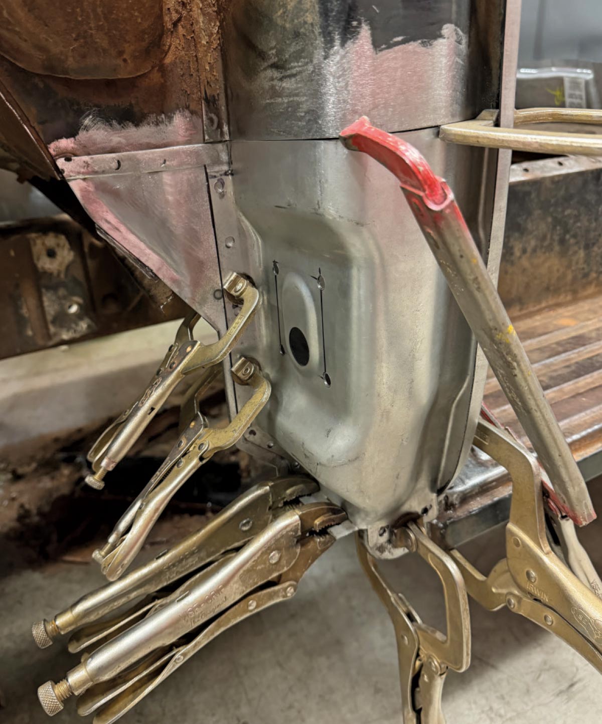 Multiple locking pliers and C-clamps hold a new front cowl repair panel in place on a truck during the metal restoration process.