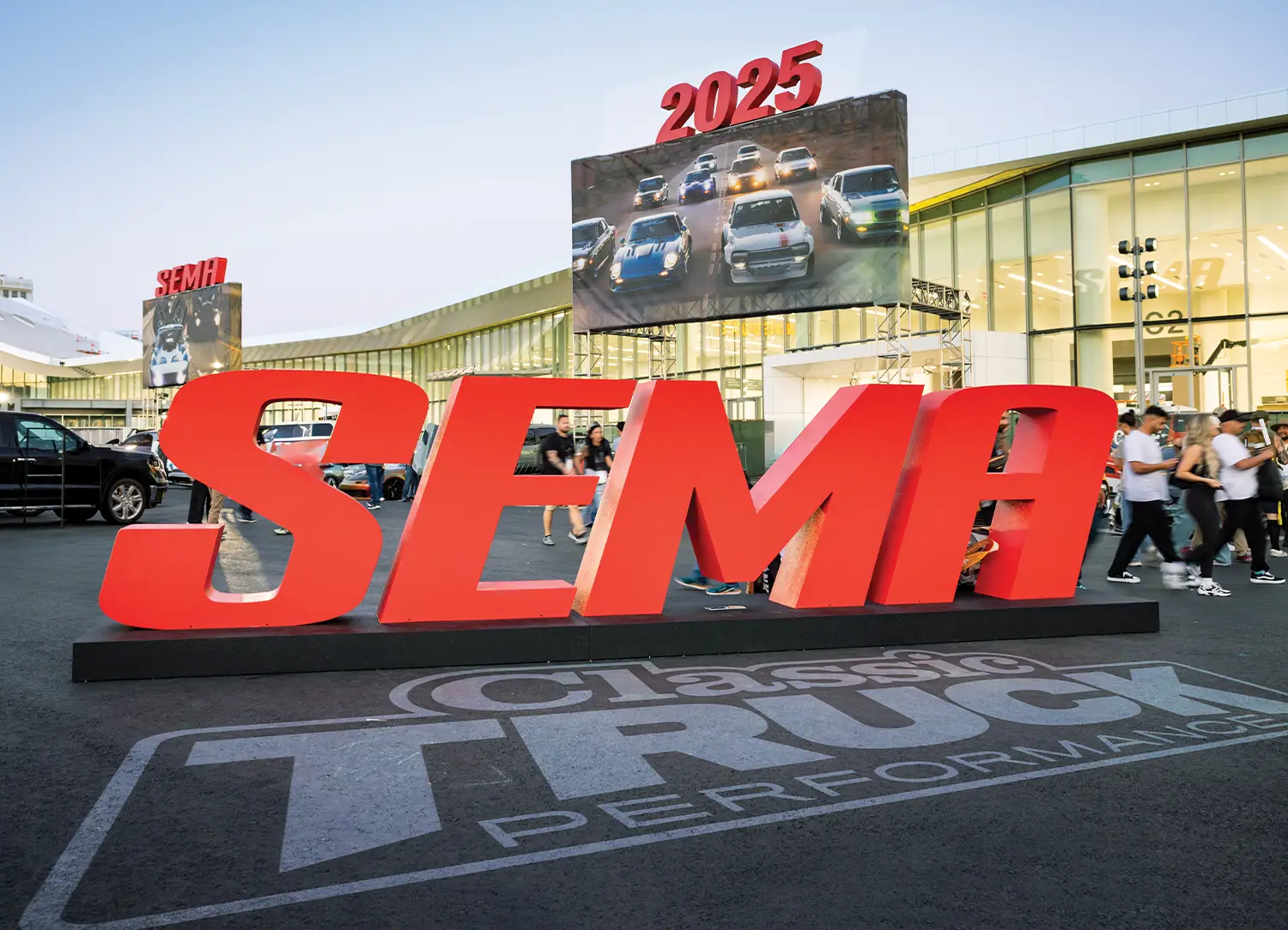 Large red 3D SEMA letters standing at the entrance of the 2025 SEMA Show in Las Vegas, with a massive "Classic Truck Performance" logo on the asphalt and a digital billboard overhead showing custom cars