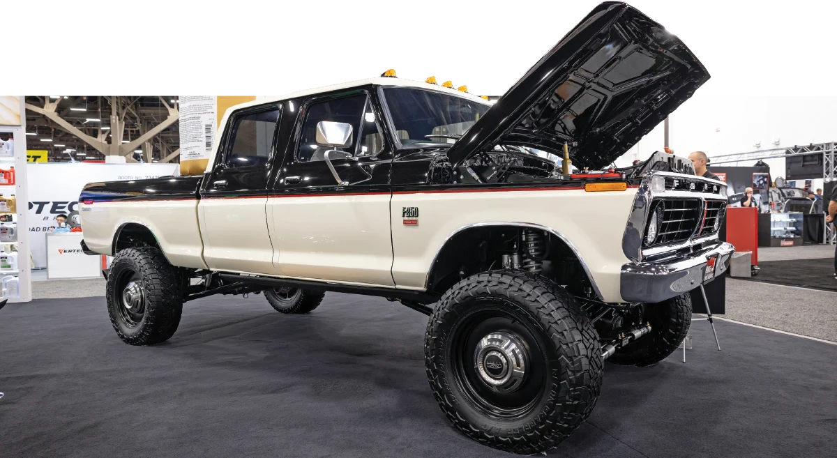 A side profile of a restored, two-tone cream and black classic Ford F-250 crew cab pickup truck on display at SEMA, featuring a lifted suspension and large off-road tires