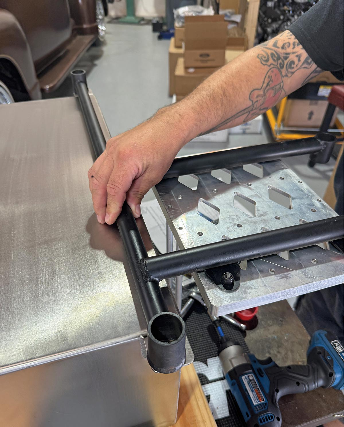 Aligning a black tubular crossmember over the stainless fuel tank mounting tabs.