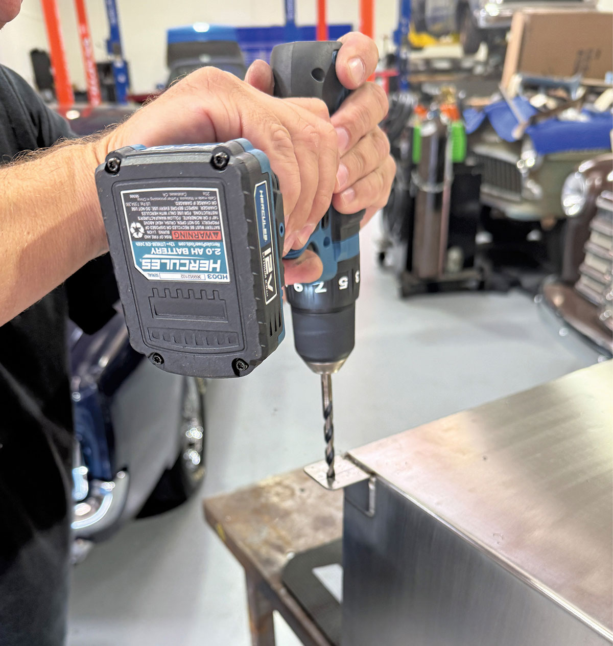 Using a Hercules power drill to create mounting holes in the fuel tank flange.