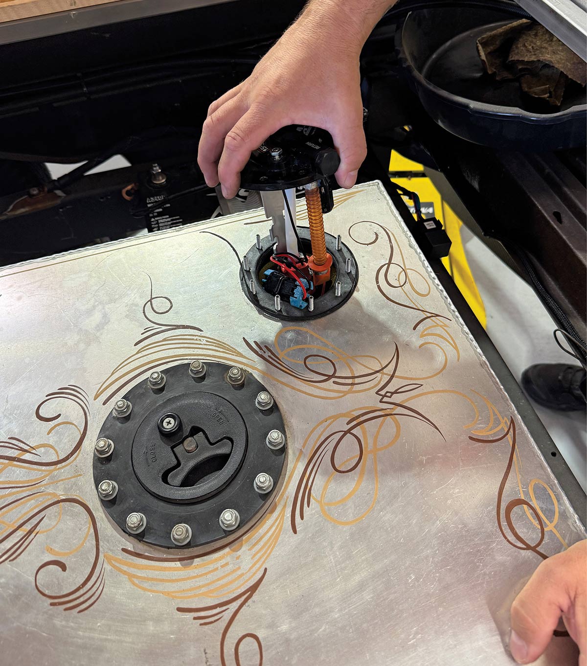 Technician lowering the fuel pump assembly into the pinstriped tank.