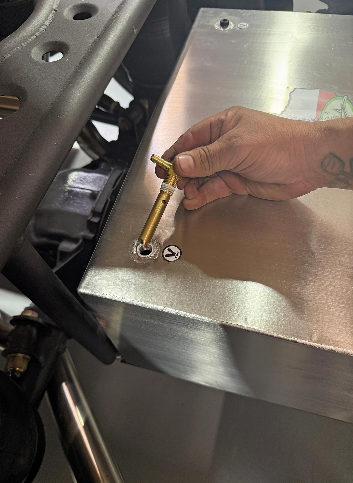 Technician hand-threading a brass rollover vent valve into the designated port on the stainless fuel tank.