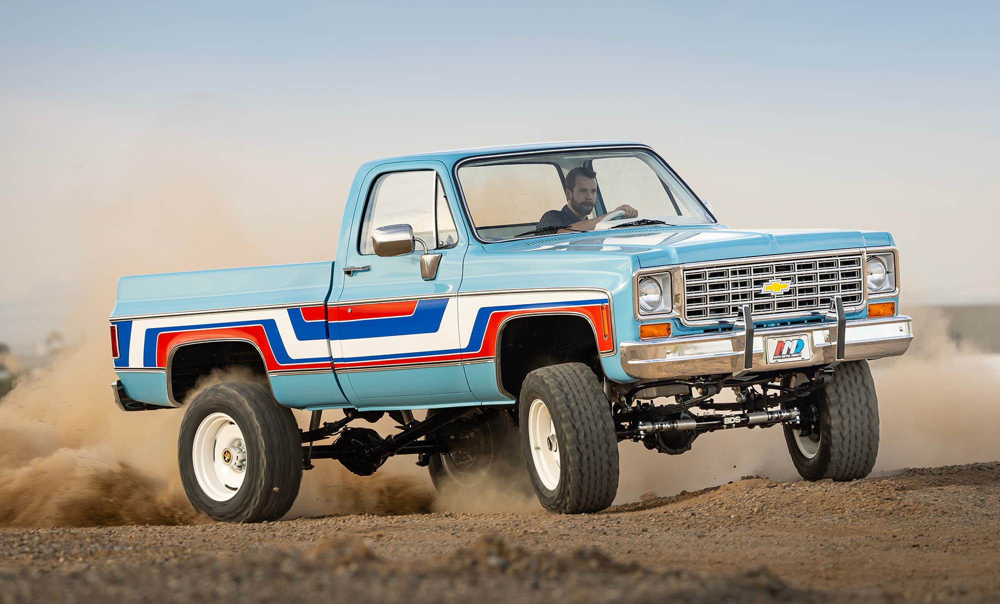 1976 Chevy K10 kicking up dust in a dirt lot.