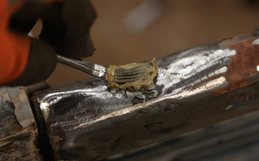 Applying flux paste to a repair area with a brush.