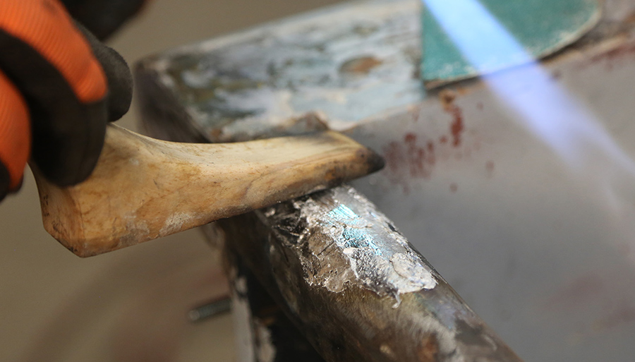 Spreading body solder using a wooden paddle and torch.