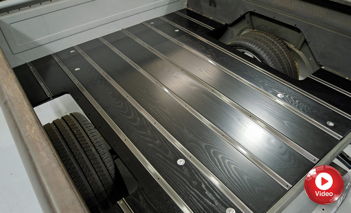 High-angle view of a custom pickup truck bed with dark stained wood flooring and polished metal trim strips.