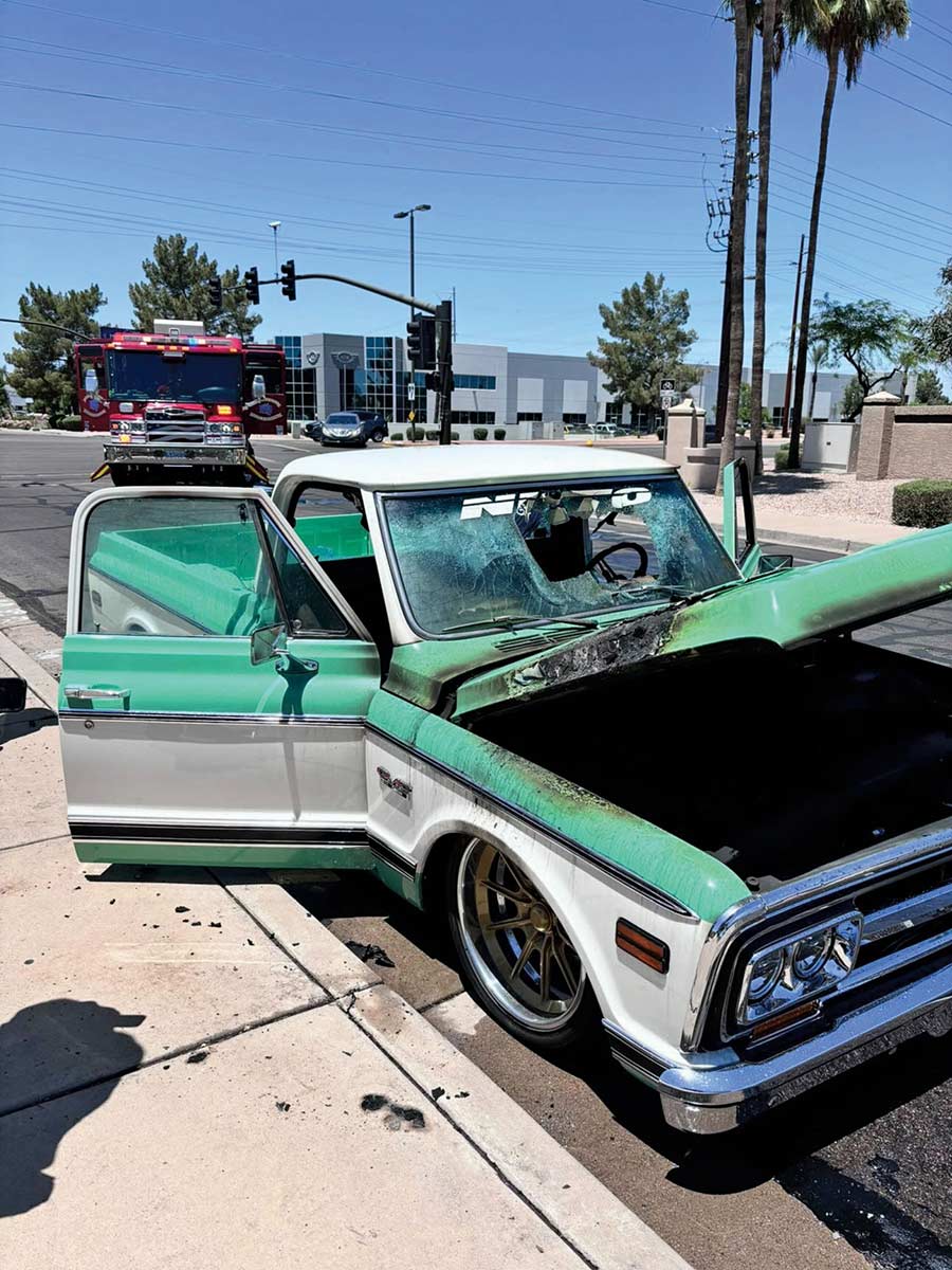 Fire-damaged classic green and white truck with shattered windshield.